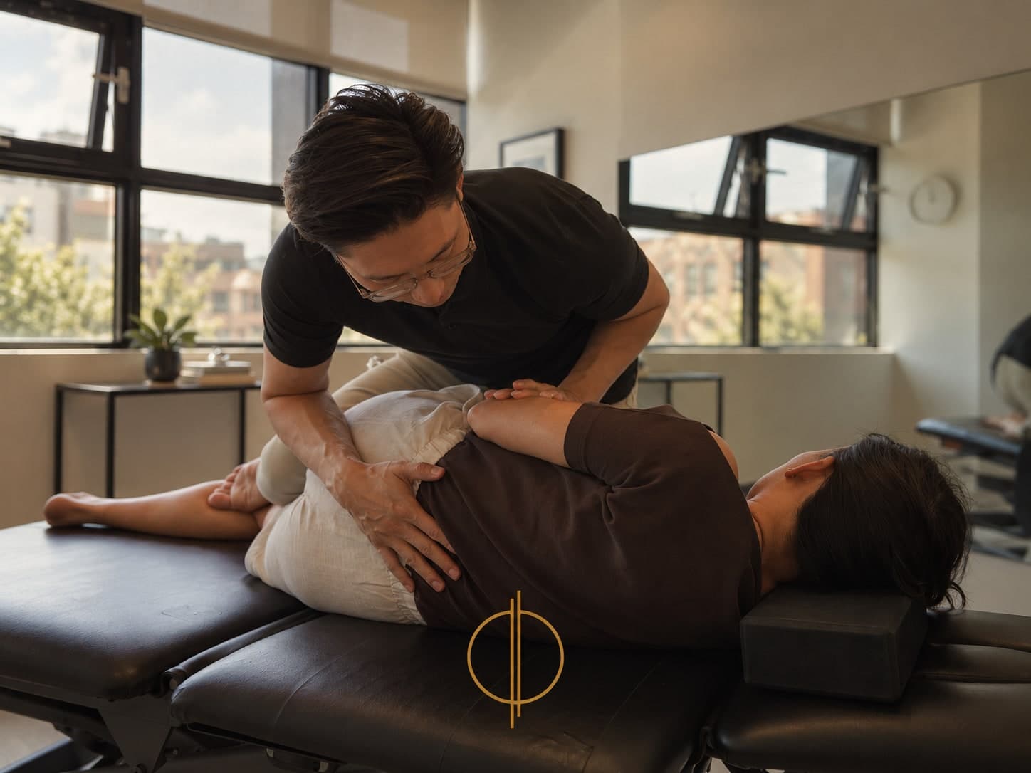 Dr. Justin Tan, chiropractor at Philo Health in Calgary, guiding a patient through a hip and knee stretch on a treatment table